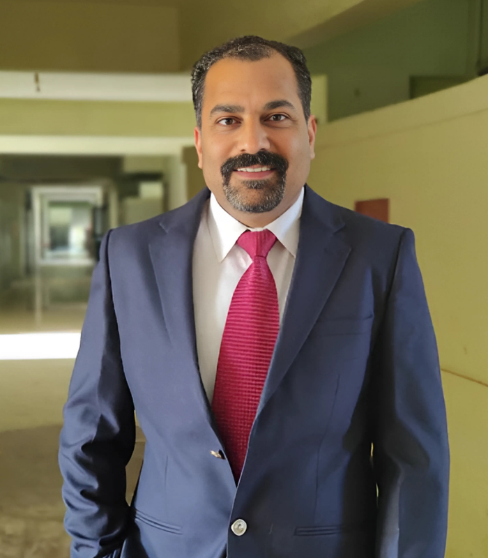 Dr. Anand Gupta, an orthopedic surgeon, standing confidently in a professional suit in a hospital corridor.